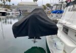 Motorboat covered with a black tarp moored at a marina, with other boats, calm water, and palm trees in the background.