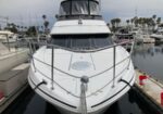 Front view of a white luxury motor yacht docked in a marina, bow facing the camera with polished railings and palm trees in the background