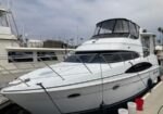 White motor yacht moored at a marina with a covered flybridge and nearby boats nearby docked alongside.
