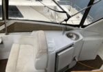 Boat cockpit with a white cushioned captain’s chair, built-in fridge, and a stainless cup holder; marina visible through the windshield.