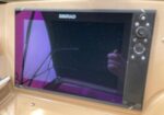 Simrad marine navigation/chartplotter mounted in a beige boat cockpit, with the screen off and the photographer's reflection visible on the panel