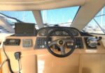 Helm of a yacht with a black steering wheel, analog gauges, and navigation screens on a tan dashboard.