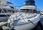 White motor yacht docked at a marina on a sunny day, showing a stainless bow rail, anchor, and mooring lines.