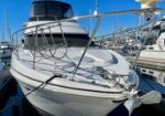 Front view of a white motor yacht docked at a marina, with stainless railing, mooring lines, and other boats in the background.