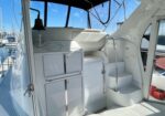 White yacht cockpit featuring built-in cabinets, a curved stairway, and helm area; marina visible through large windows.