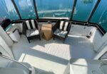 Two black wicker chairs with striped cushions flank a small table on a boat deck, with blue water visible beyond.