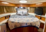 Cozy yacht cabin with a large bed, seashell-patterned quilt and decorative pillows, wood cabinets along the walls, a small TV, and a circular skylight above.
