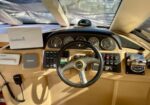 Boat cockpit helm with steering wheel, round gauges, Garmin device on the left, beige dashboard, and throttle controls on the right.