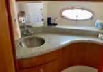 Compact boat bathroom with curved granite counter, sink, mirror, and toilet on a wooden cabinet base