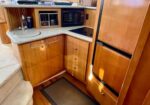 Compact wooden boat galley with a fridge, microwave, sink, and curved countertop.