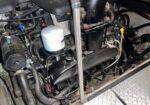 Close-up of a diesel engine in an engine bay, showing a white cylindrical filter, hoses, and metal components.