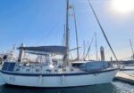 Sailboat docked at a marina on a sunny day with an Italian flag flying from the mast.