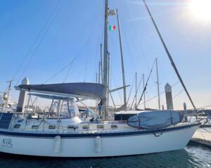 Sailboat docked at a marina on a sunny day with an Italian flag flying from the mast.