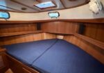 Cozy boat cabin with blue cushioned bed, wood paneling, and small portholes along the walls.