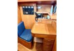 Wooden boat cabin navigation station with a blue cushioned bench, curved desk, and mounted radio/communication panels.