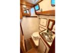 Compact boat head with wooden cabinets, stainless sink, and toilet in a cozy marine bathroom.