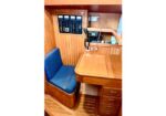 Wood-paneled boat cabin with a small desk, blue seat, and a wall-mounted control panel (radio and gauges).