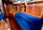 Wood-paneled sailboat cabin with a blue cushioned bench, pillows, and built-in cabinets along the walls.