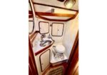 Small boat head with a stainless sink, storage cabinets, and a marine toilet; wood trim and floor grate visible.