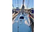 View from the bow of a white sailboat in a sunny marina, with other boats docked nearby.