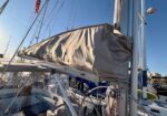 Sailboat at a marina with its mainsail neatly covered and rigging visible.