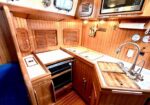 Compact wooden boat galley with stove, oven, sink, and microwave on a varnished countertop.