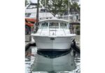 White motor yacht docked at a marina, bow facing the camera with reflections in calm water.