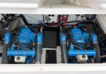 Twin blue marine engines in a boat's engine room, with hoses, wiring, and battery banks around them.