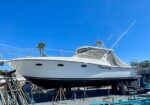 White motor yacht lifted on supports in a dry dock with a bright blue sky above.
