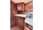 Compact boat galley: wooden cabinets, microwave, and small fridge beneath a light countertop with a yellow towel and bottled water on the counter.