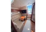 Cozy boat cabin lounge with beige leather seating around a small wooden table and wood-paneled walls, door to the deck on the right.
