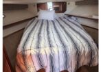 Bed in a compact boat cabin with a striped white and navy comforter and two white pillows