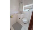 Small white bathroom with a wall-mounted sink, cabinet, porthole window, and a gray bath mat on the floor.