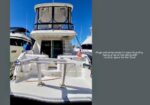 Rear view of a white motor yacht docked at a marina, with a swim platform and davit on the stern under a blue sky