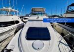 White luxury motor yacht at a marina, bow sunpad with dark cushions; blue promo label reads 'Expansive Bow Sunpad, your front-row seat to sun and open water!'