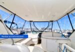 Interior of a motor yacht cockpit with hardtop and full enclosure, white seating, and panoramic marina views.