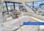 Luxurious yacht lounge with white leather seating and large windows overlooking a marina. The caption reads that the flybridge is ideal for entertaining underway or at the dock.