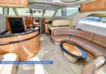 Luxurious yacht salon with curved tan leather seating, round glass table, and wooden cabinetry overlooking large windows