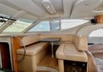 Luxurious boat cabin with beige leather seating around a small table, wood accents, and large porthole windows in a yacht salon.