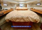 Owner's cabin on a yacht featuring an island queen bed, warm wood cabinetry, and porthole windows with beige bedding.