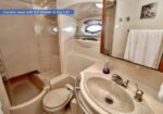 Compact boat head with sink, toilet, shower enclosure, towel rack, and porthole window (yacht bathroom).
