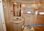 VIP day head and shower on a yacht: compact white bathroom with sink, mirror, cabinet, portholes, and shower stall.