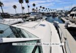Yacht at a marina with palm trees in the background; a safety banner on the deck reads: 'Wide Side Decks make for safe Passage to the bow!'