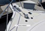 Close-up of the boat bow showing an electric windlass and anchor chain on a white deck, near the bow pulpit, at a marina dock