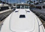 Front view of a white motor yacht docked in a marina, with other boats on either side and blue sky above.