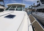 View along the bow of a white luxury motor yacht docked at a marina, with stainless railings, nearby boats, and palm trees against a clear blue sky.