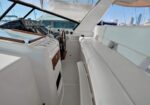 Cockpit of a white luxury yacht with helm, steering wheel, and bench seating; marina in the background.