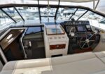 Boat cockpit with steering wheel, instrument panel, and helm controls; views of marina through windshield.