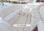 White cushioned U-shaped seating on a yacht deck with a small central table; water and shoreline visible in the background.