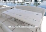 White cushioned seating around a large foldable table on a yacht deck by the marina, set for outdoor dining.